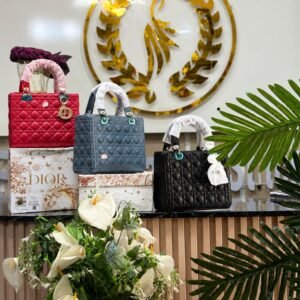 Three Dior handbags in red, blue and black colors on display with flowers