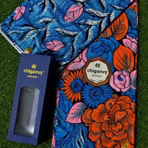 Vibrant floral Ankara fabric with blue, pink, orange and black colors, accompanied by a matching box on green grass.